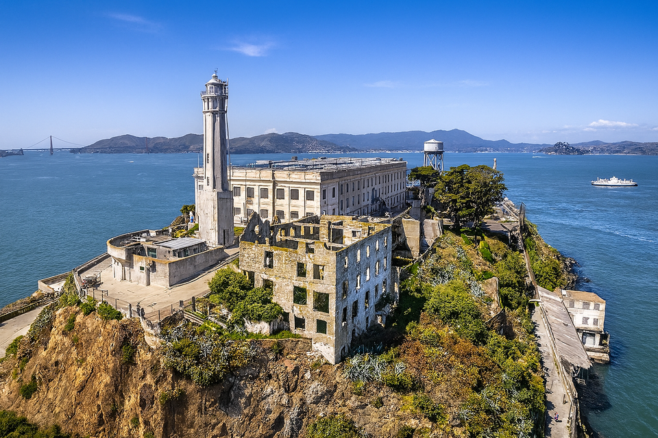 Aerial view of Alcatraz Island with historic prison buildings, lighthouse, and ruins, surrounded by San Francisco Bay.